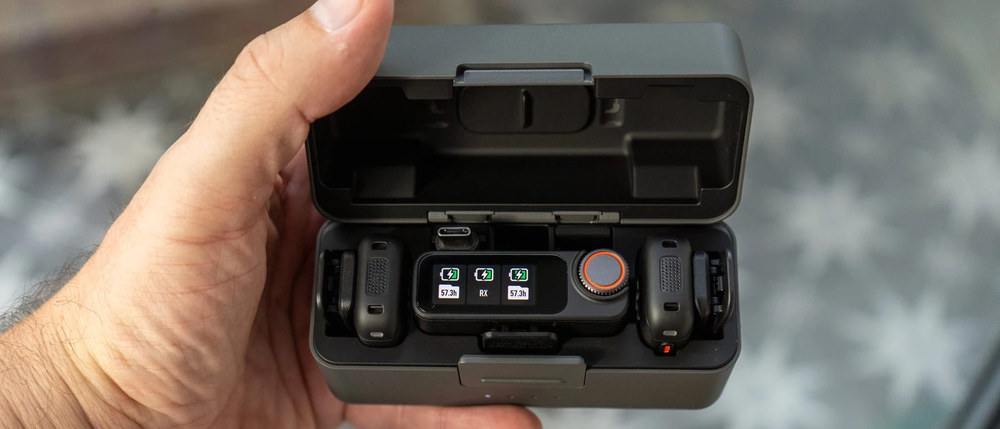 Відкритий зарядний кейс DJI Mic 3 у руці, на екрані приймача світяться три зелені індикатори заряду та залишок запису 57.3 години.