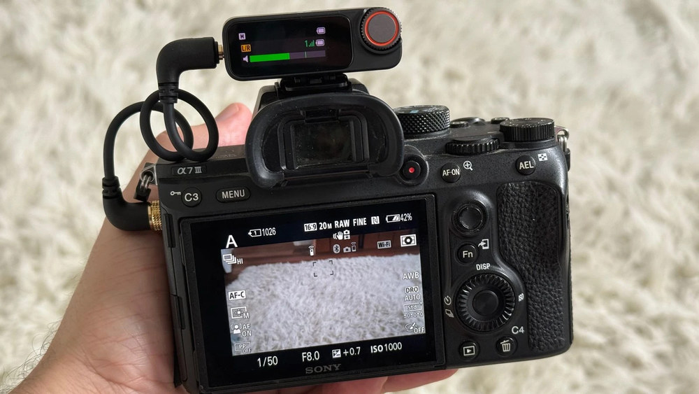 Приймач DJI Mic 3 закріплений у гарячому башмаку камери Sony a7 III і підключений аудіокабелем, на екрані приймача видно поточний рівень сигналу.